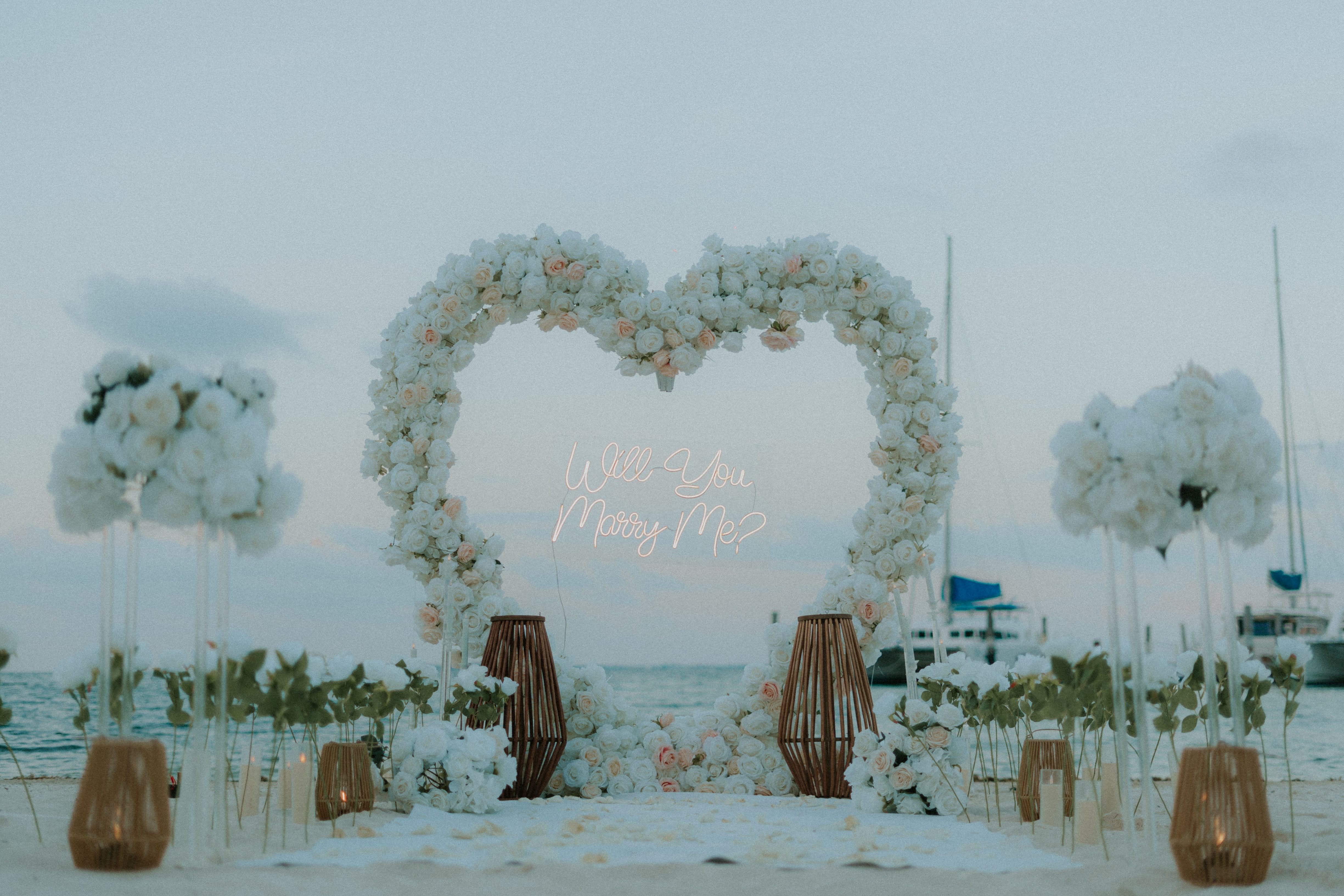 Romantic beach engagement in Playa del Carmen featuring a lush tropical floral arch with white and pink roses on a private stretch of sand.