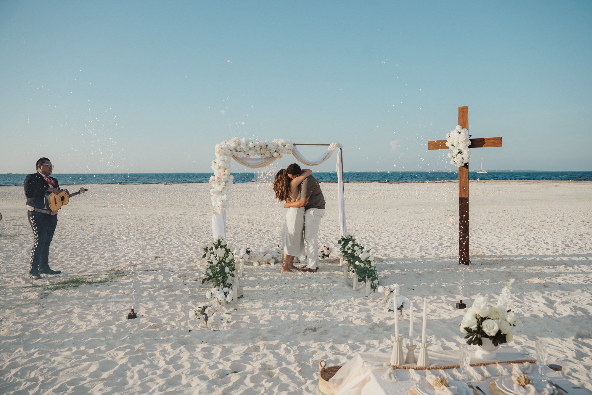 Stunning beach proposal at golden hour in Cancun with a minimalist wooden arch, warm lanterns, and soft sunlight reflecting off the ocean waves.