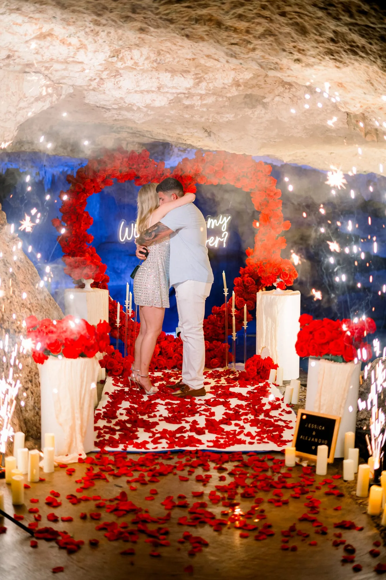 A just-engaged couple embracing beneath sparklers inside a candlelit cenote