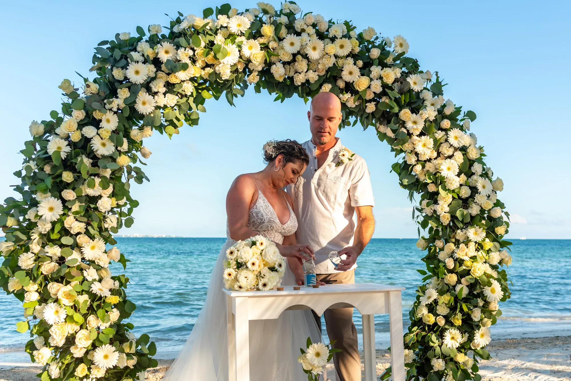 Couple during a seaside ceremony beneath a floral arch