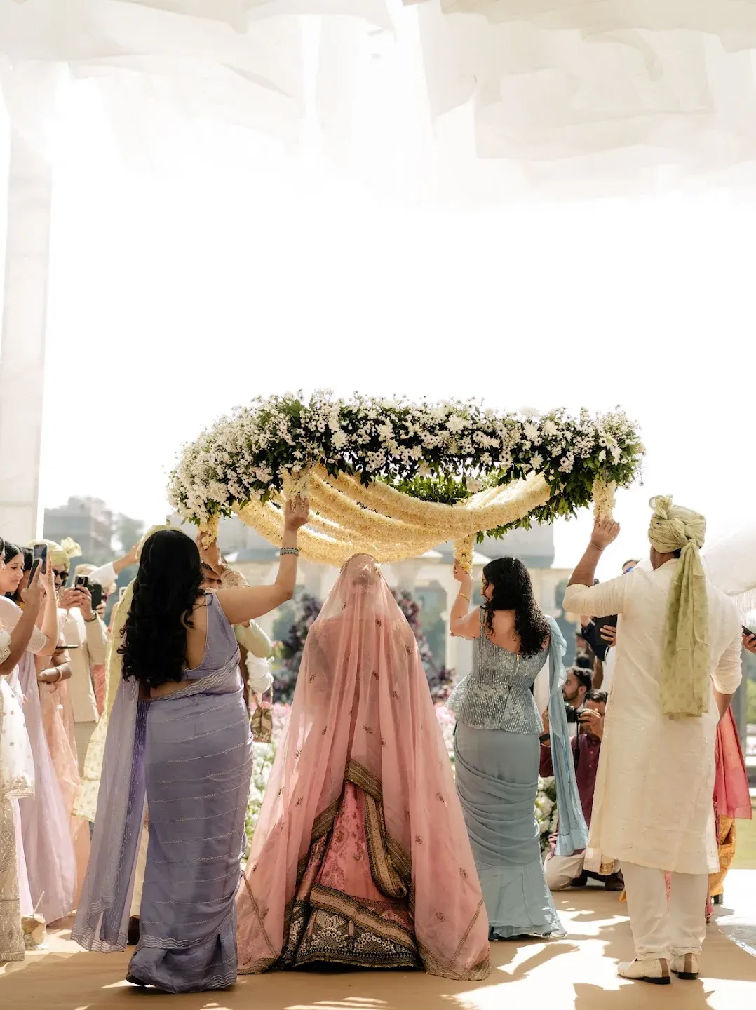 Wedding guests accompanying the bride beneath a floral canopy